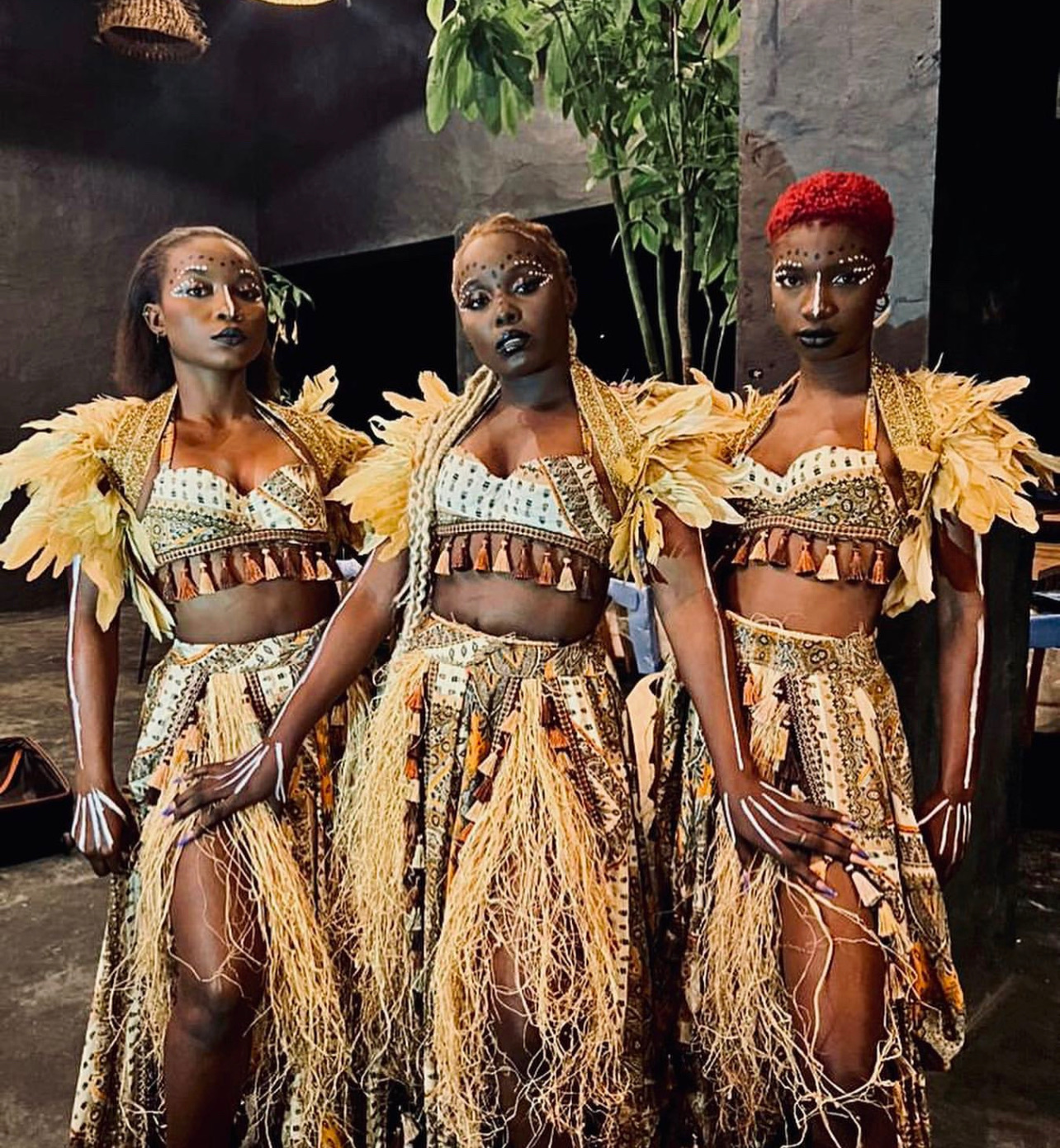 Three performers in gold feathered shoulder pieces and hand-beaded festival costumes