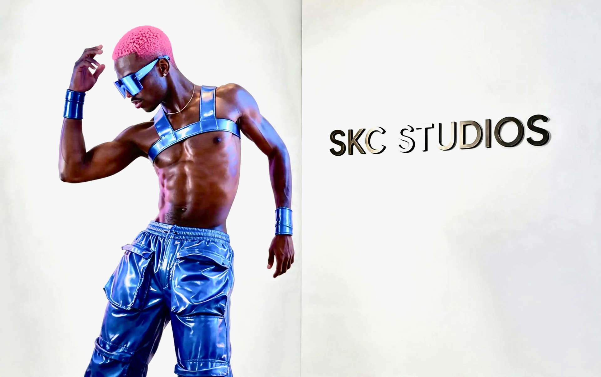 Dancer in metallic blue harness and cargo trousers beside the SKC Studios wall sign
