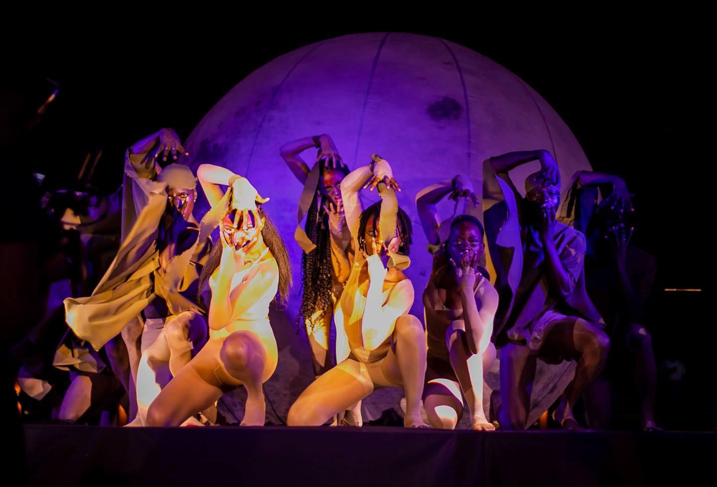 Ensemble posed before a giant moon set piece